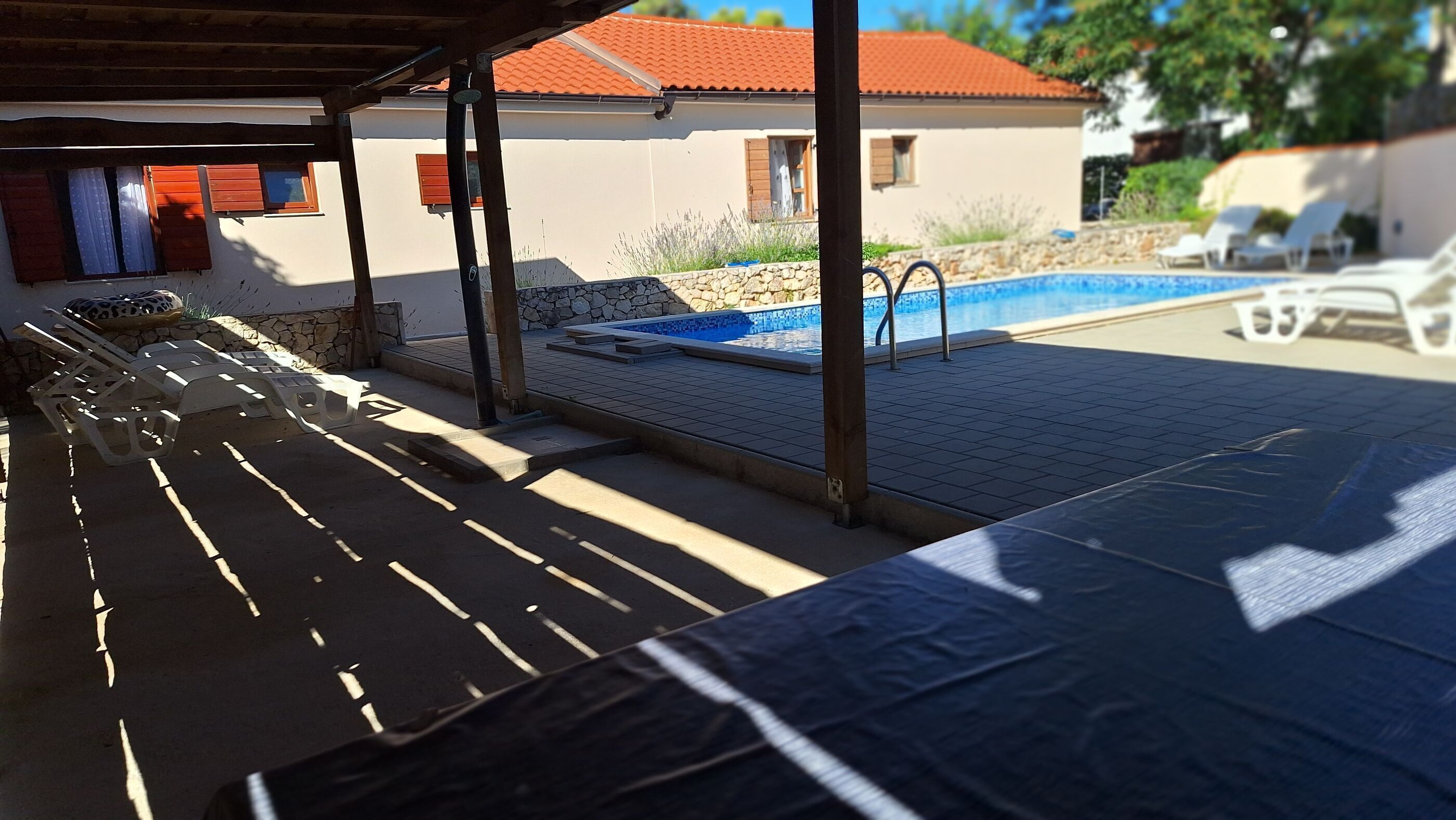Ein überdachter Außenbereich mit Pool, Liegestühlen und einer Steinmauer.
