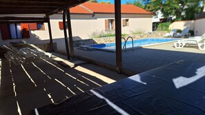 Ein überdachter Außenbereich mit Pool, Liegestühlen und einer Steinmauer.
