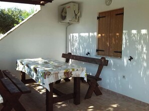 A covered outdoor dining area with a table set for two, a wooden bench, and a wall-mounted air conditioning unit. - Apartments Laura and Romano With Pool (Vir)