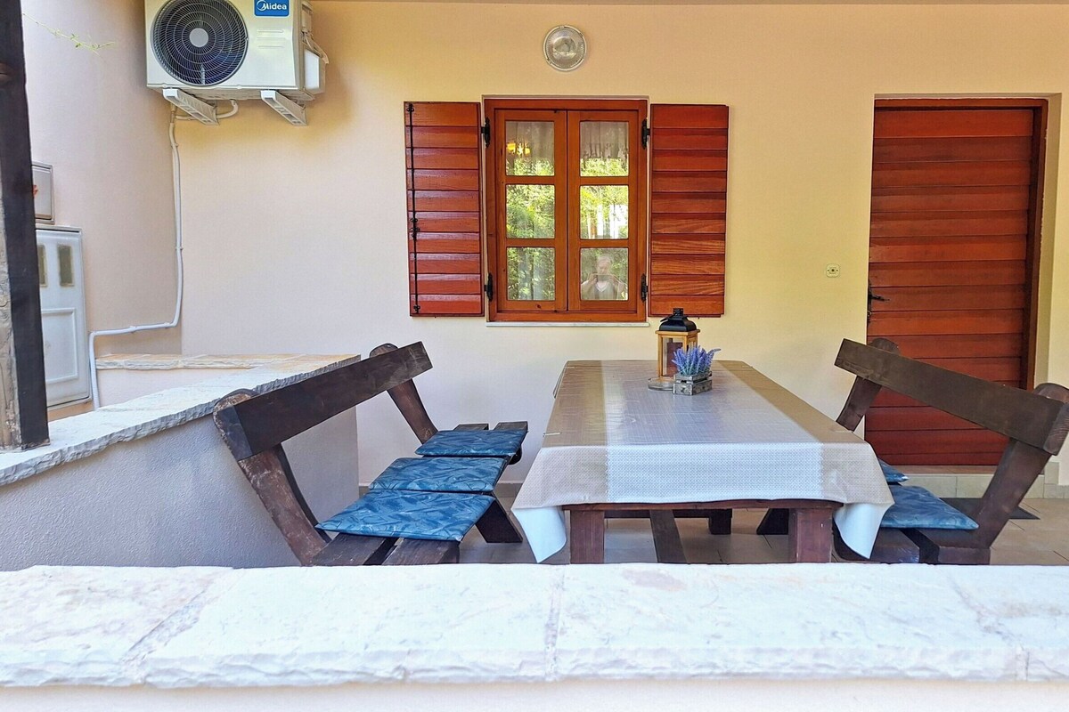 A room with a table, two chairs, a window with wooden shutters, and an air conditioning unit.