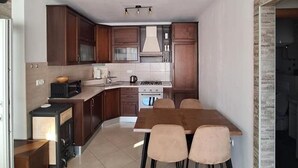 A modern kitchen with dark wooden cabinets, a central island, and a dining area with four chairs. - Apartment Goran (Makarska)