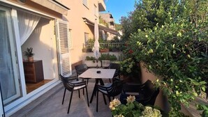 A patio with a table and chairs, a potted plant, and a building with balconies. - Apartment Goran (Makarska)