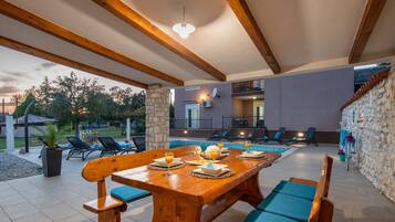 Un área de comedor al aire libre con una mesa y sillas de madera, una piscina y un muro de piedra.