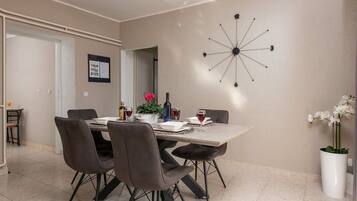 A dining area with a table set for four, chairs, a wall clock, and a potted plant.