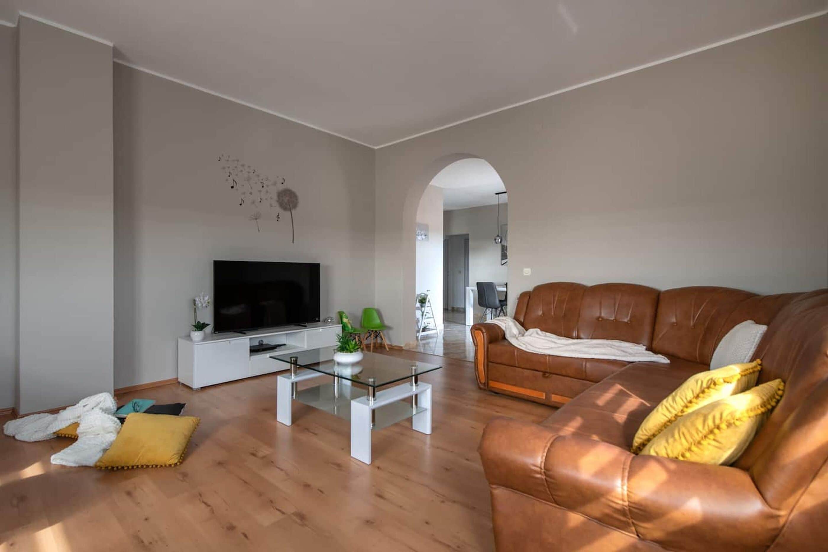 Ein Wohnzimmer mit einem braunen Ledersofa, einem Glastisch, einem Flachbildfernseher und einer weißen Unterhaltungseinheit.