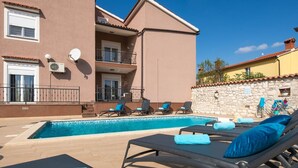 A swimming pool with lounge chairs and towels, a stone wall, and a building with balconies and satellite dishes. - House Villa Lara (Marcana)