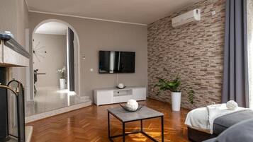 A modern living room with a flat-screen TV, a white console table, a grey sofa, and a potted plant.