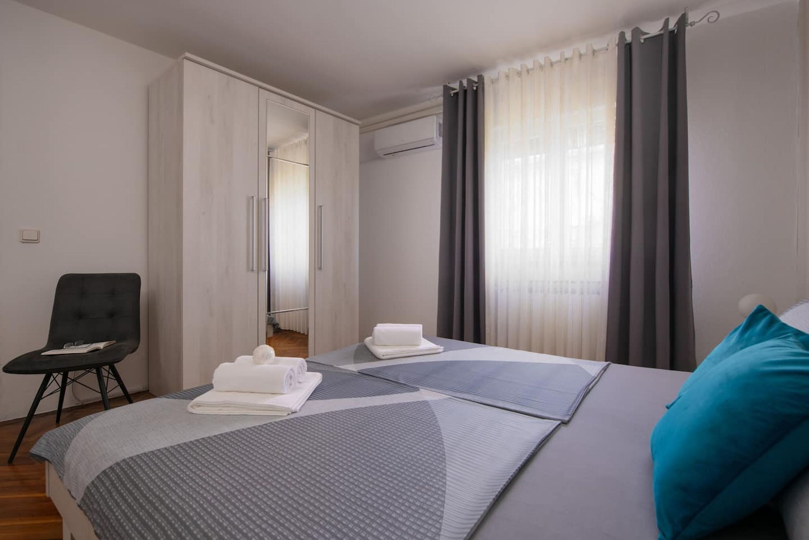 A hotel room with a bed, a chair, a wardrobe, and a window with curtains.