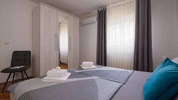 A hotel room with a bed, a chair, a wardrobe, and a window with curtains.