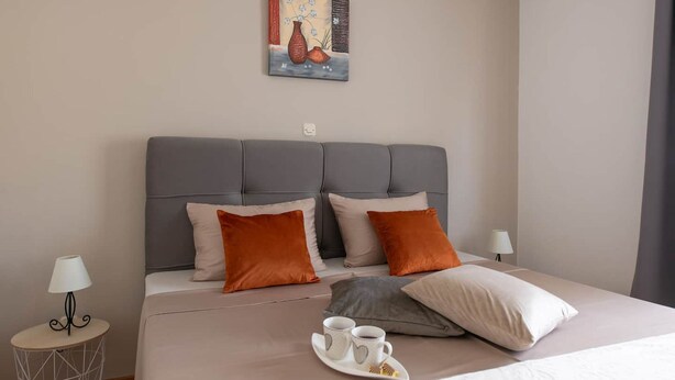 A neatly arranged hotel room with a grey upholstered headboard, a painting above the bed, and a tray with cups on the bed. - House Villa Lara (Marcana)