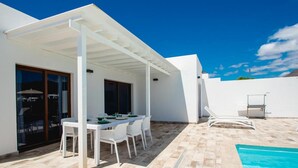 A modern outdoor dining area with a white table and chairs, a covered patio, and a pool. - Villa Montane 10 - Three Bedroom Villa, Sleeps 6 (Playa Blanca)