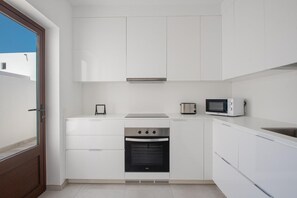 Une cuisine compacte avec des meubles blancs, un four encastré, un four à micro-ondes et un grille-pain.