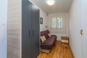 A small room with a wooden floor, a bed with a brown cover, a wardrobe, and a window with curtains. - Apartments Steps From the Sea (Senj)