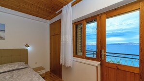 Ein Schlafzimmer mit Bett, Holzboden, einem Fenster mit Meerblick und einer Holztür.