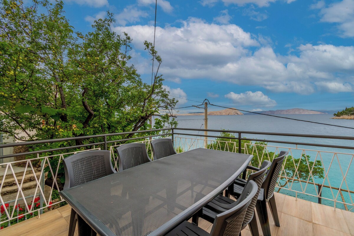 Eine Terrasse mit Tisch und Stühlen, mit Blick auf ein Gewässer und die Ferne.