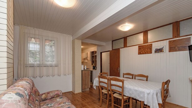 Ein gemütliches Zimmer mit einem blumigen Sofa, einem Esstisch mit Stühlen, einer Küchenzeile und einem an der Wand befestigten Fernseher.