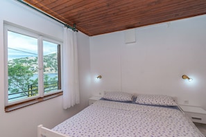 Ein Schlafzimmer mit einem Bett, zwei Nachttischen, einem Fenster mit Blick und einer Holzbalkendecke.