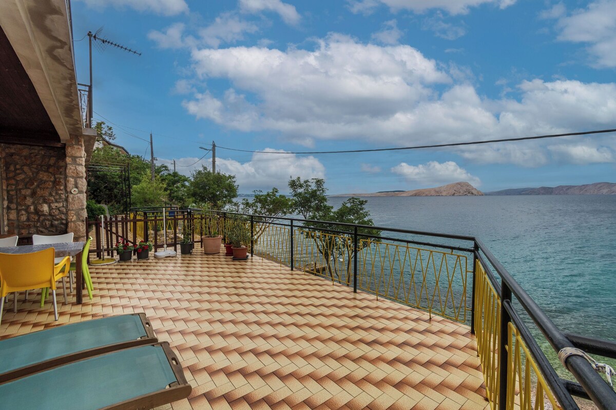Eine Terrasse mit Fliesenboden, Gartenmöbeln und einem Geländer mit Blick auf ein Gewässer.