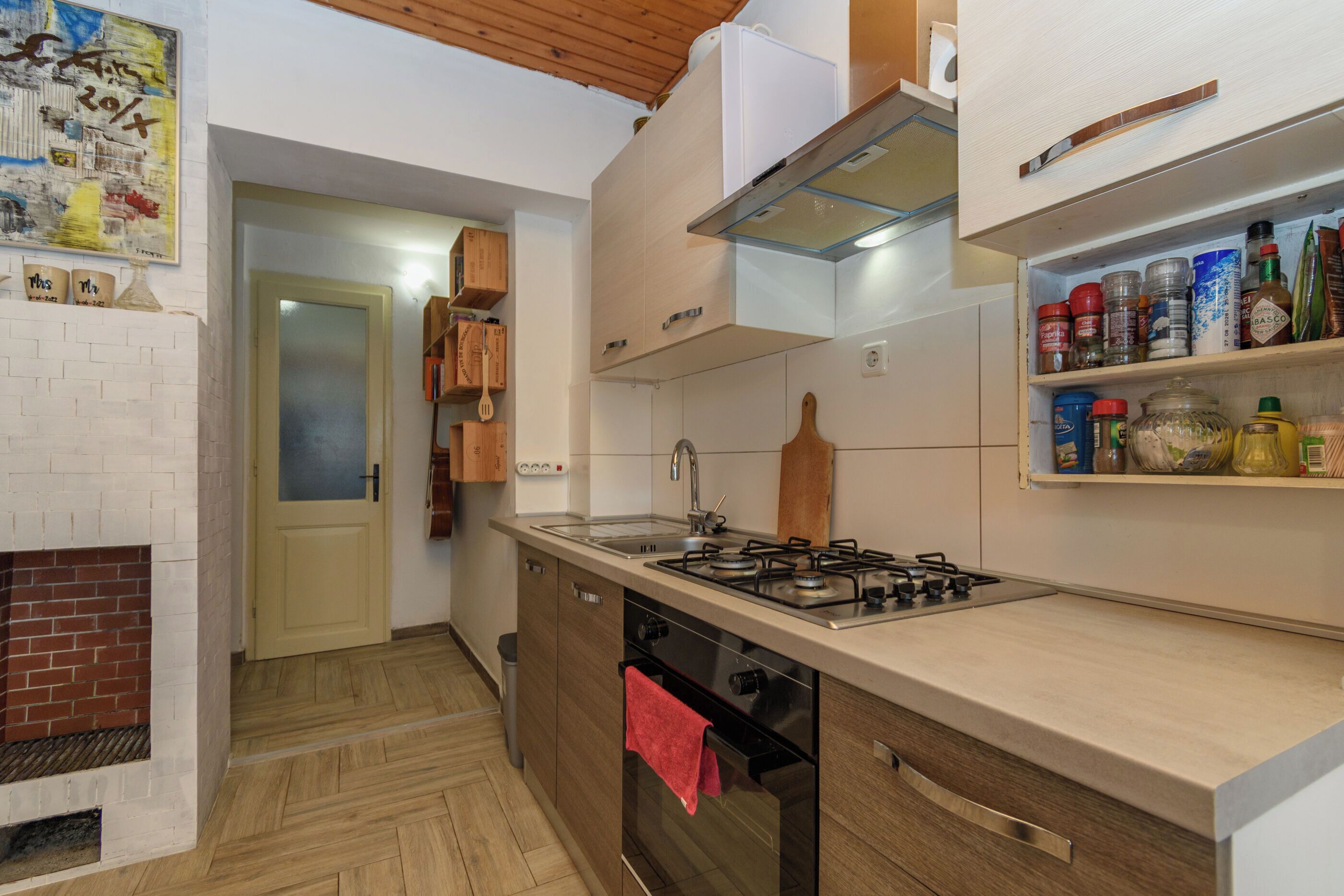 Una cocina con estufa a gas, horno y un armario de madera con un perchero para ollas.