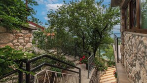 Eine Steintreppe führt zu einem Balkon mit Blick auf Bäume und einen klaren Himmel.