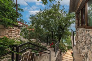 Eine Steintreppe führt zu einem Balkon mit Blick auf Bäume und einen klaren Himmel.