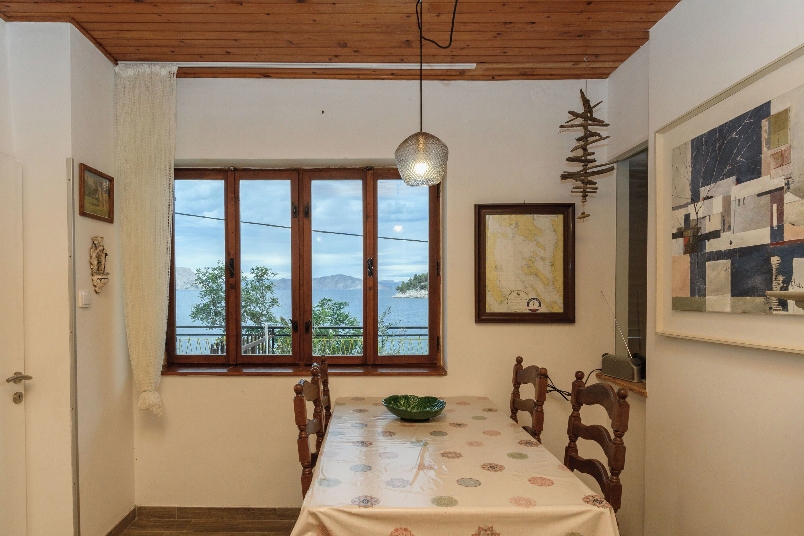 Un comedor con una mesa, sillas, una lámpara colgante, un ventanal con vistas y obras de arte en las paredes.