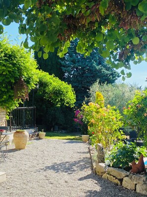 Ein Garten mit Kiesweg, Topfpflanzen, einer Steinmauer und einem Metallzaun.