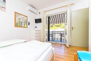 Ein Schlafzimmer mit Bett, Fernseher, Spiegel und einer Schiebetür zum Balkon.