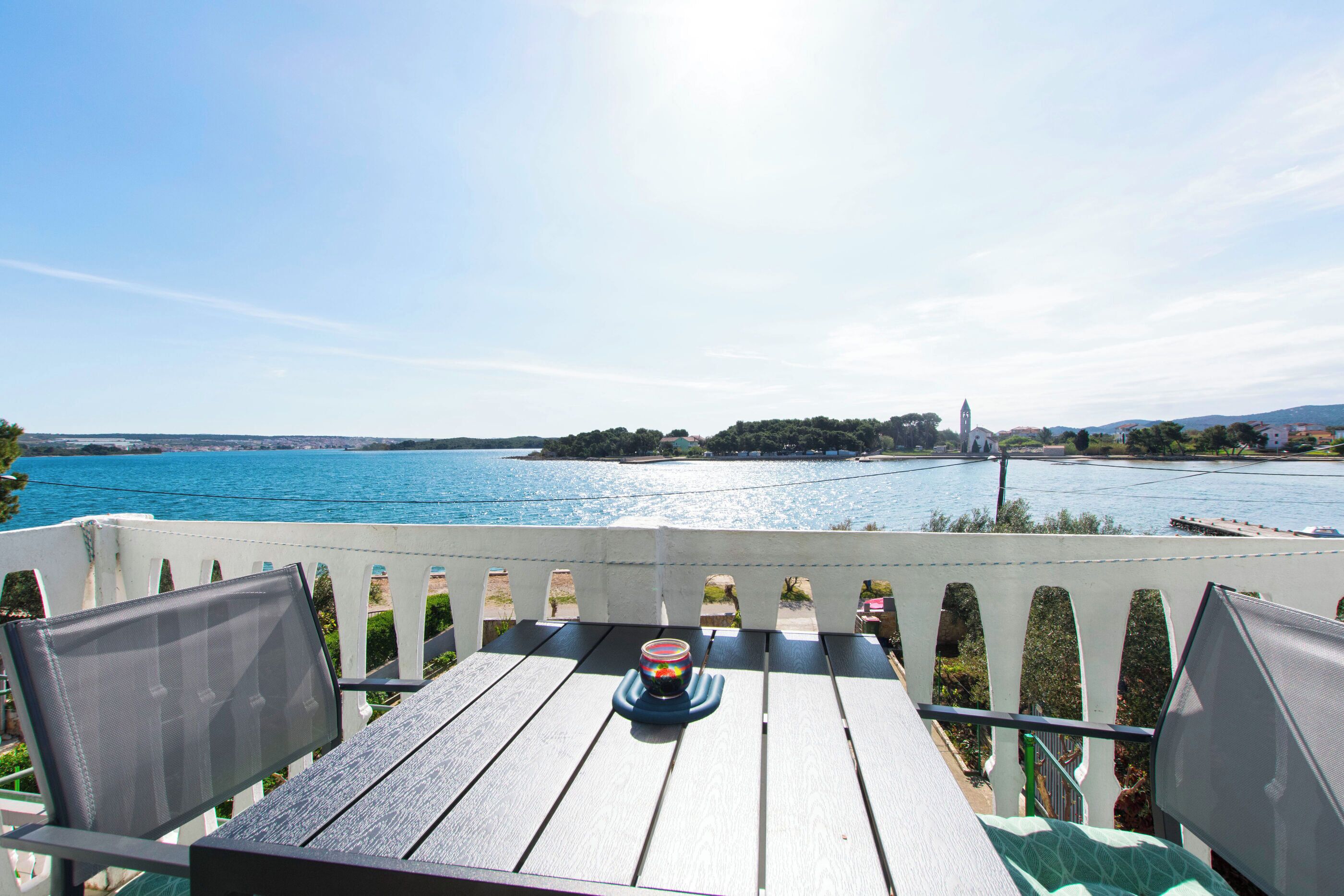 A balcony with a table, chairs, and a view of a body of water and distant land.