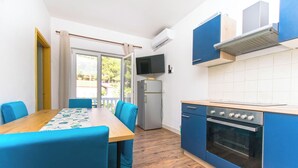 Eine kompakte Küche mit Esstisch, Stühlen, einem Kühlschrank, einem Backofen und einem an der Wand befestigten Fernseher.