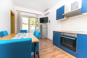A compact kitchen with a dining table, chairs, a refrigerator, an oven, and a TV mounted on the wall. - Apartments Sweet Pasman (Pasman)