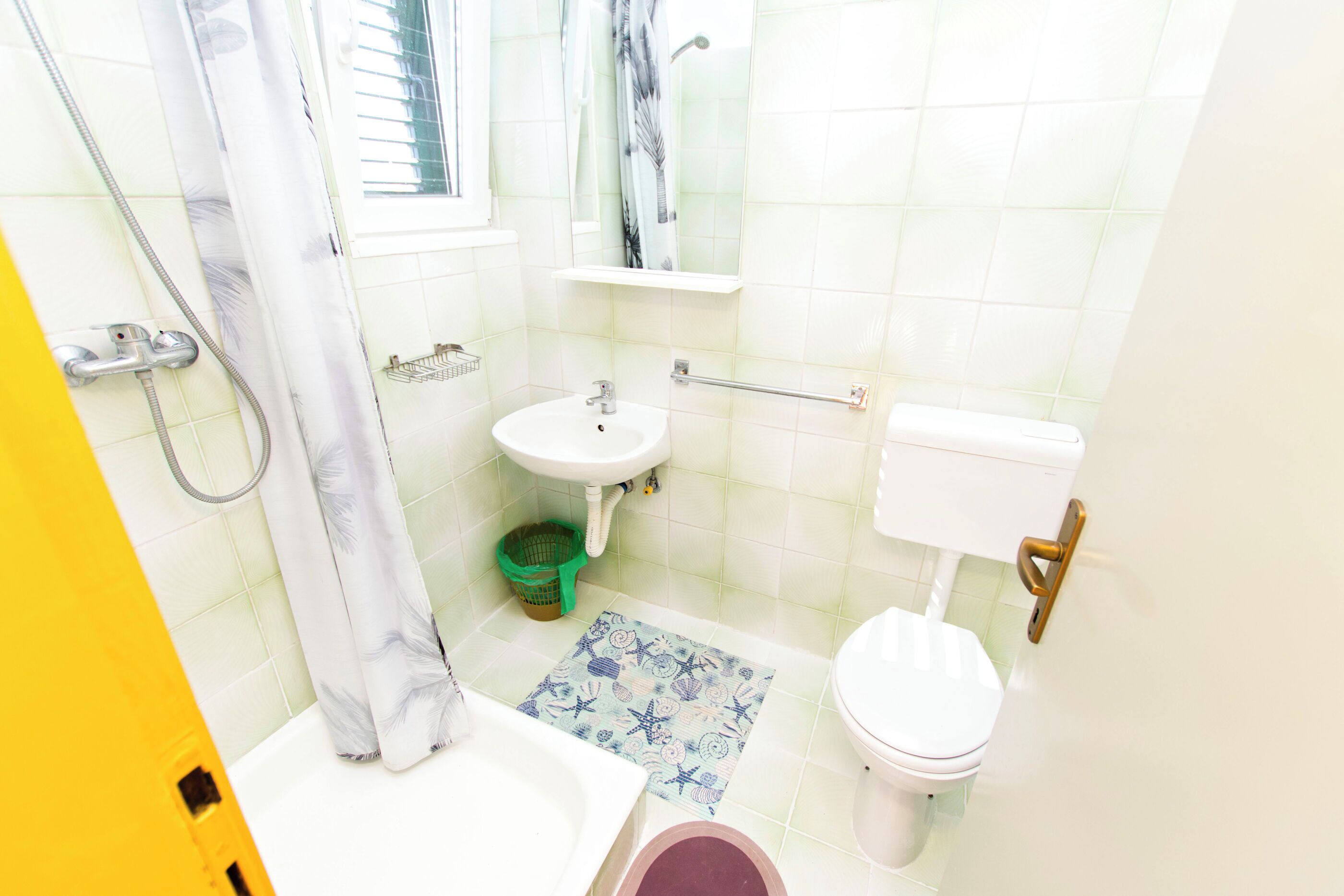 Un baño con ducha, lavabo, inodoro y un ventanal pequeño.