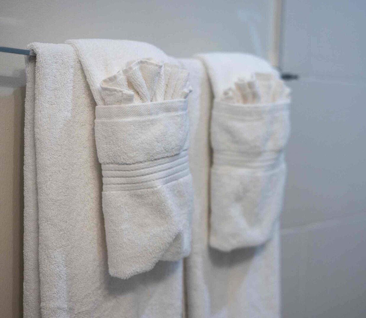 Dos toallas blancas colgadas en una barra de metal dentro de un baño.
