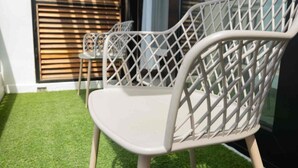 A white outdoor seating area with a chair and a small table, set against a backdrop of wooden blinds and a glass door. - VIA Braemar Suites - with roof-top pool (Kingston)
