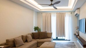 A living room with a sectional sofa, an ottoman, a ceiling fan, and a flat-screen TV mounted on the wall. - VIA Braemar Suites - with roof-top pool (Kingston)