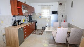 A kitchen with wooden cabinets, a refrigerator, a stove, and a dining area with chairs. - Apartments Plavsic (Novi Vinodolski)