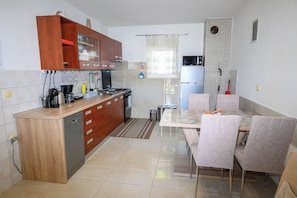 A kitchen with wooden cabinets, a refrigerator, a stove, and a dining area with chairs. - Apartments Plavsic (Novi Vinodolski)