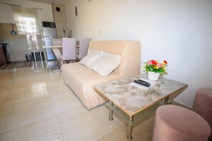 Ein Wohnzimmer mit einer Couch, einem kleinen Tisch mit Blumenvase, einer Küchenzeile im Hintergrund und einem Badezimmer mit Handtuchhalter.