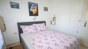 A bedroom with a bed, a headboard, a wall-mounted lamp, and two framed pictures. - Apartments Plavsic (Novi Vinodolski)