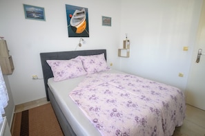 A bedroom with a bed, a headboard, a wall-mounted lamp, and two framed pictures. - Apartments Plavsic (Novi Vinodolski)