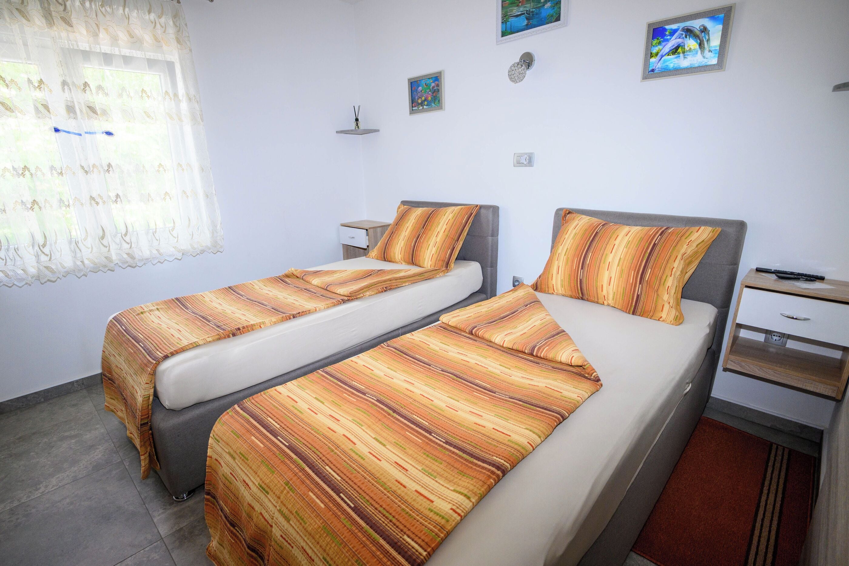 A double room with two beds, a small bedside table, a nightstand, and a wall-mounted shelf.