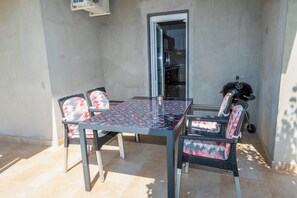 Eine Terrasse im Freien mit Tisch, Stühlen, einem Grill und einer Tür, die zu einer Küche führt.