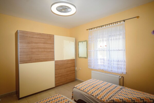 A bedroom with a bed, a wardrobe, a mirror, and a window with curtains. - Apartments Plavsic (Novi Vinodolski)