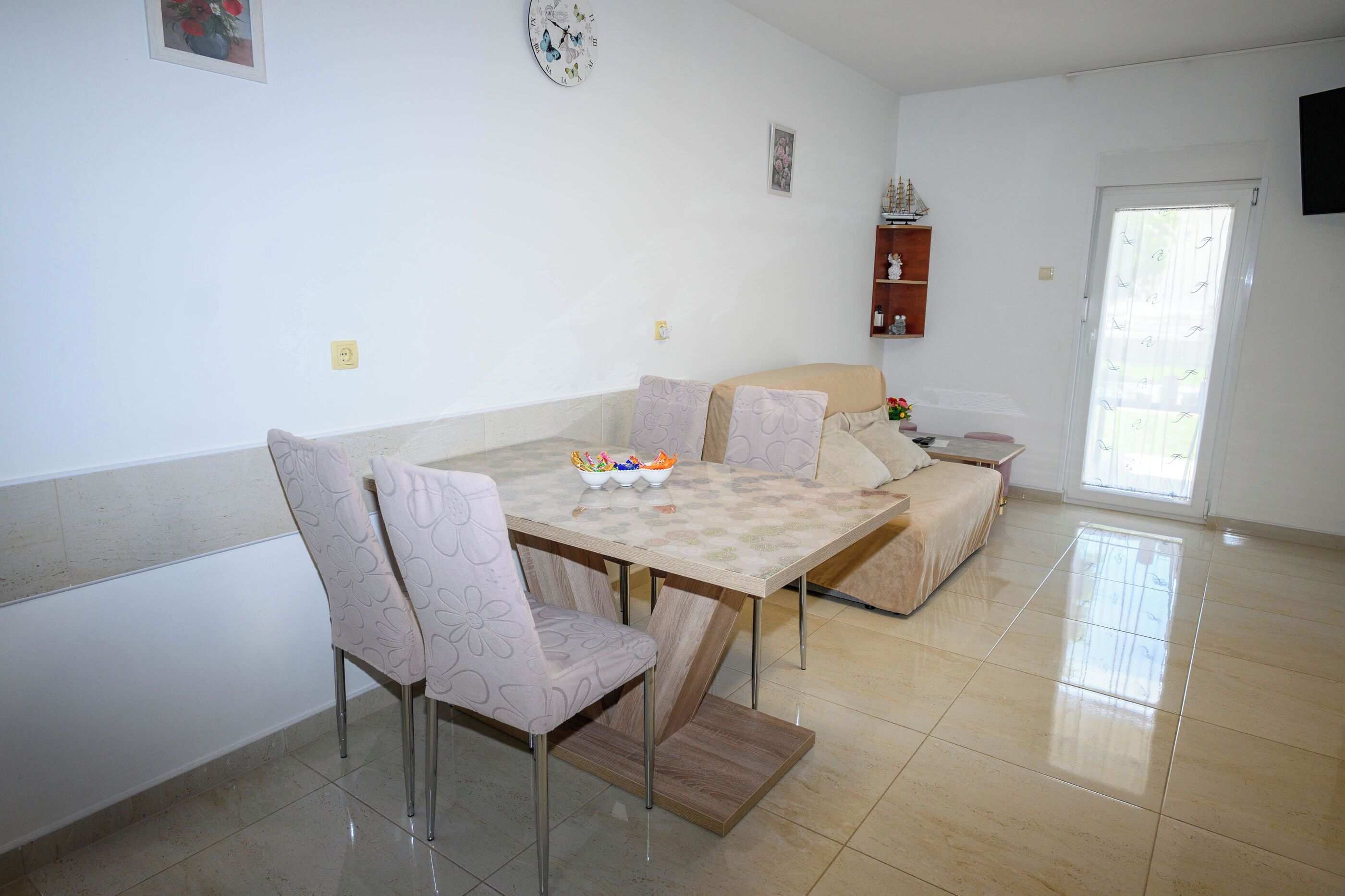 A dining area with a table, chairs, a sofa, and a small shelf with decorative items.