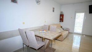 A dining area with a table, chairs, a sofa, and a small shelf with decorative items. - Apartments Plavsic (Novi Vinodolski)