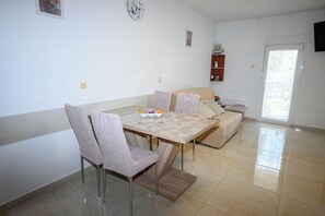 A dining area with a table, chairs, a sofa, and a small shelf with decorative items. - Apartments Plavsic (Novi Vinodolski)