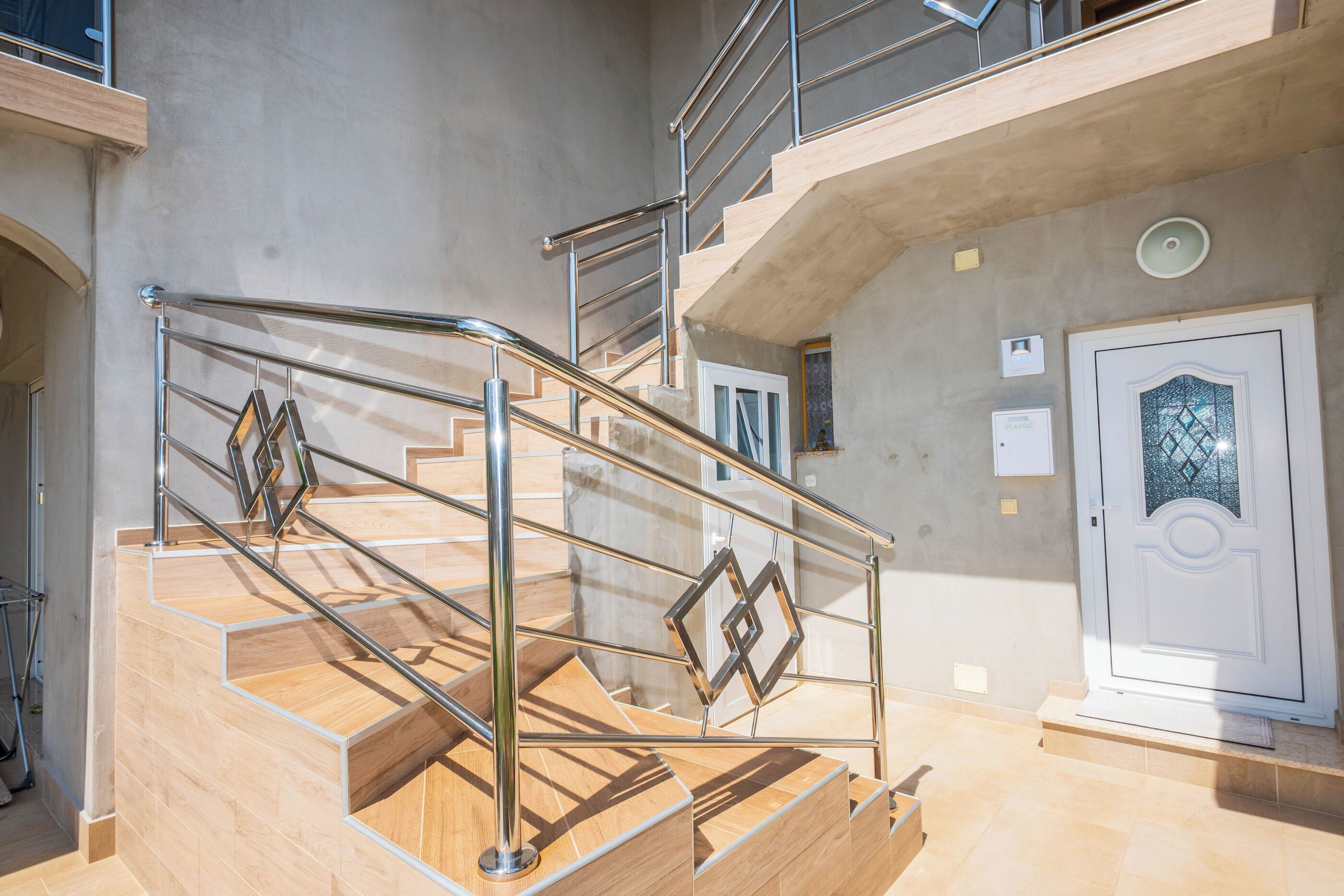 Un interior de varios niveles con escalera, barandales de metal y una puerta con panel de vidrio decorativo.