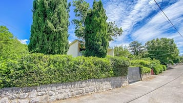 A residential area with stone walls, tall trees, and a paved road.