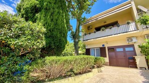 Ein zweistöckiges Gebäude mit Balkon, Garage und einem gepflegten Garten.