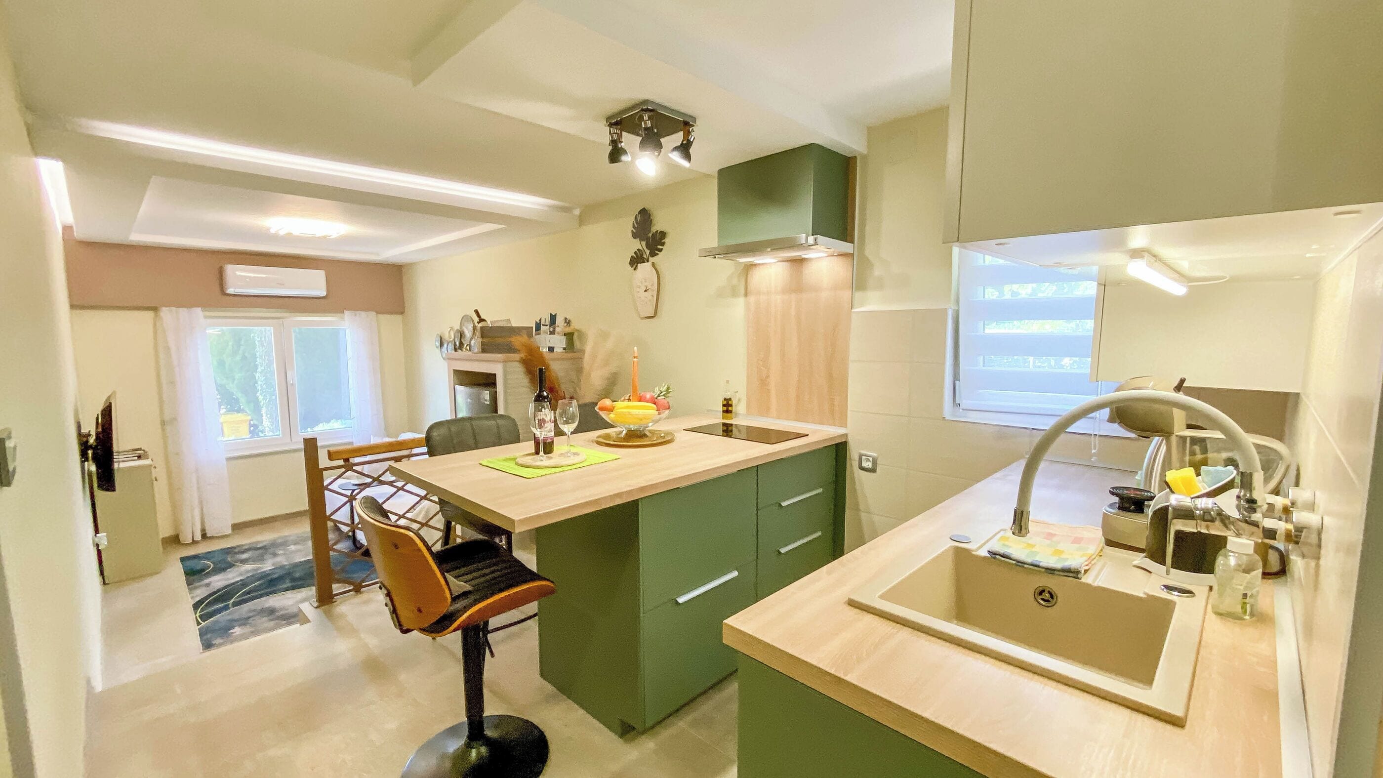 A modern kitchen with a central island, a dining area with a chair, and a sink with a mirror.